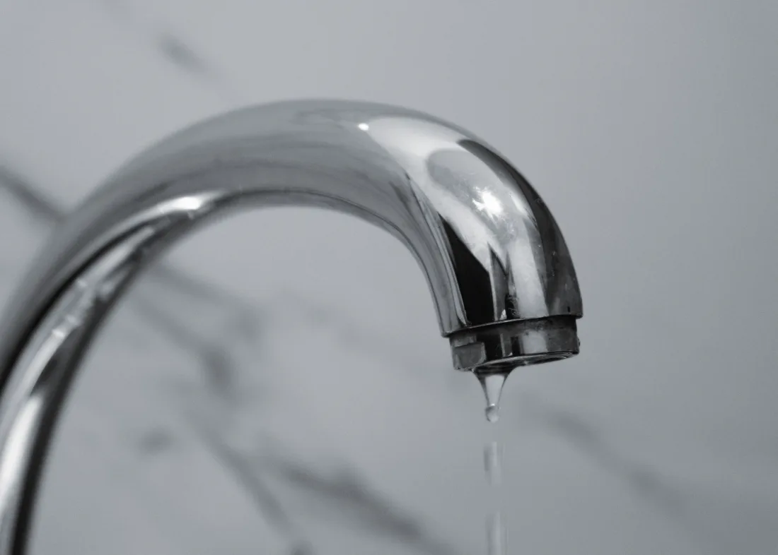 Caño de grifería cromada con una gota cayendo, sobre un fondo de mármol.