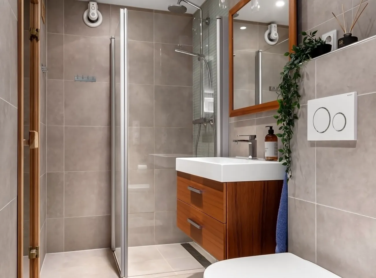 Baño terminado con pared de gran formato gris, mueble de madera y ducha con mampara.